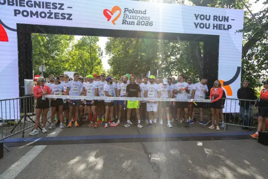 Grupa biegaczy na starcie Poland Business Run 2026, z transparentem i kibicami w tle.