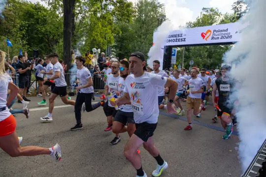 Biegacze startują w Poland Business Run 2026, otoczeni dymem i kibicami.