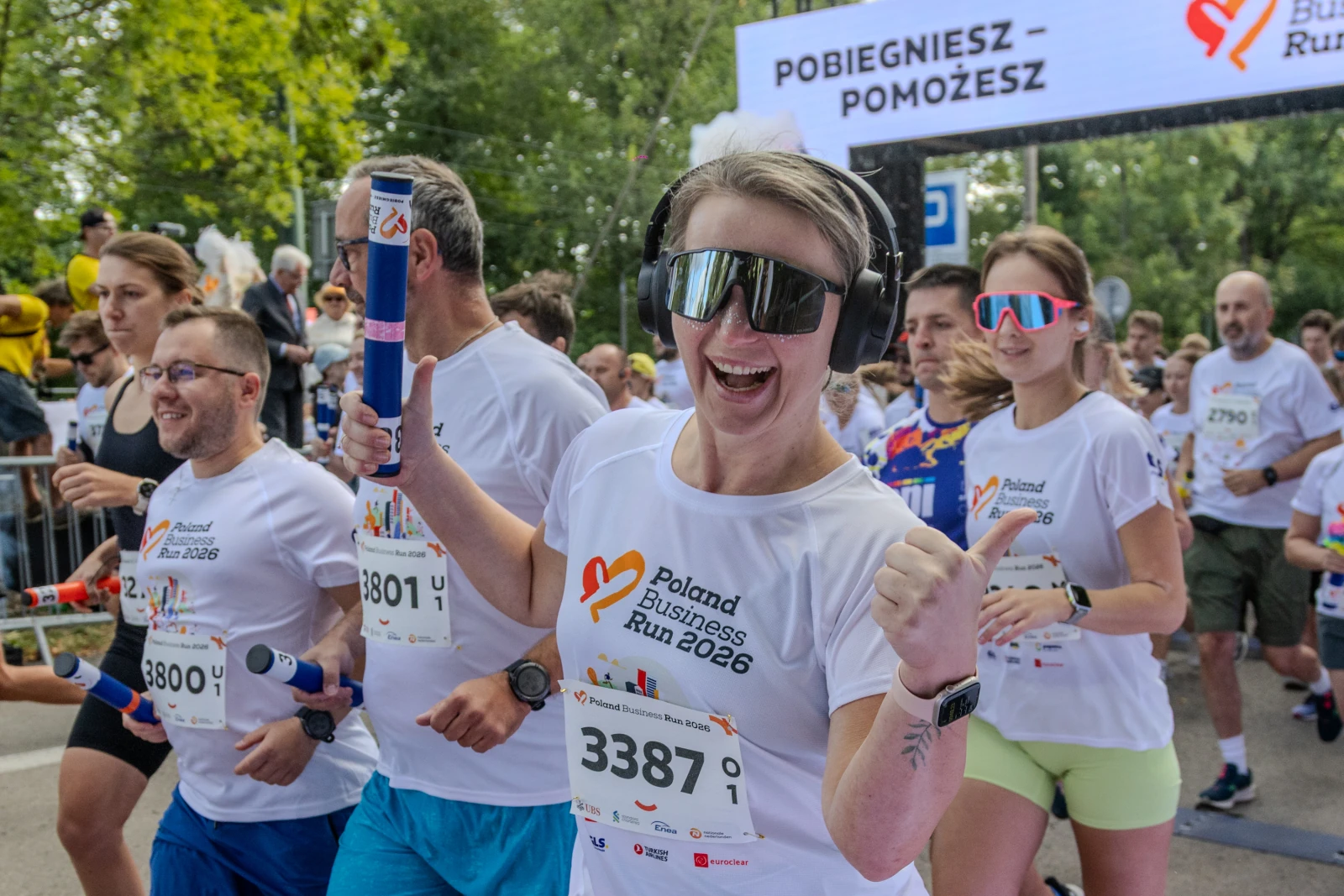 Biegacze w koszulkach z logo Poland Business Run, radosna uczestniczka z słuchawkami i butelką w ręku.  Autor: Bogusław Świerzowski