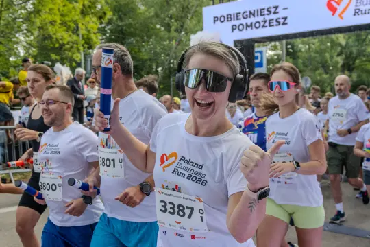 Biegacze w koszulkach z logo Poland Business Run, radosna uczestniczka z słuchawkami i butelką w ręku.