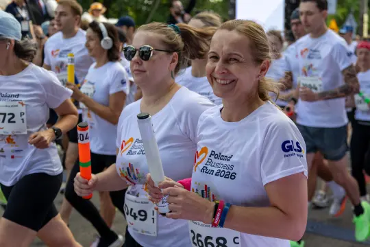 Biegacze w koszulkach z logo Poland Business Run 2026, uśmiechnięte twarze, atmosfera radości.