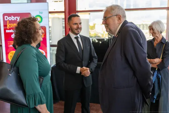 Spotkanie kilku osób w eleganckim otoczeniu, rozmowy i interakcje towarzyskie.