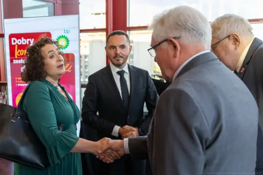 Kobieta w zielonej sukience wita się z mężczyzną w garniturze, w tle reklama BP.