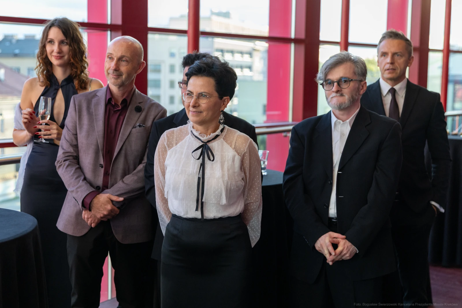 Grupa elegancko ubranych ludzi na przyjęciu, stojących w sali z dużymi oknami.  Autor: Bogusław Świerzowski