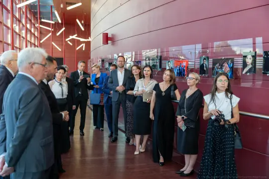 Grupa ludzi w eleganckich strojach podczas wydarzenia w nowoczesnym wnętrzu.