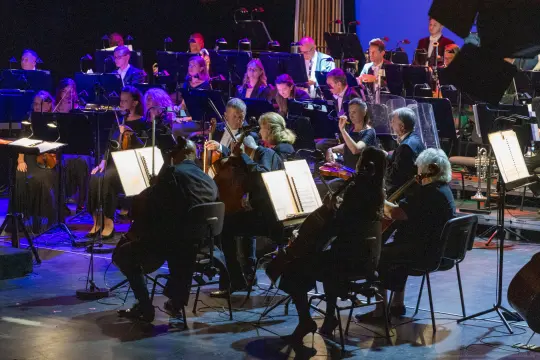 Orkiestra grająca na scenie, muzycy z instrumentami w skupieniu.
