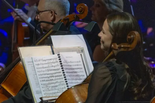 Muzycy orkiestry podczas występu, z nutami na stojaku.