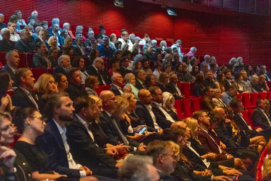 Tłum ludzi siedzących na widowni w sali teatralnej.