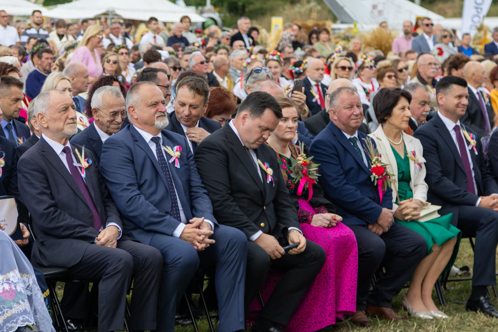 Grupa ludzi w eleganckich strojach siedzących na uroczystości plenerowej.  Autor: Bogusław Świerzowski