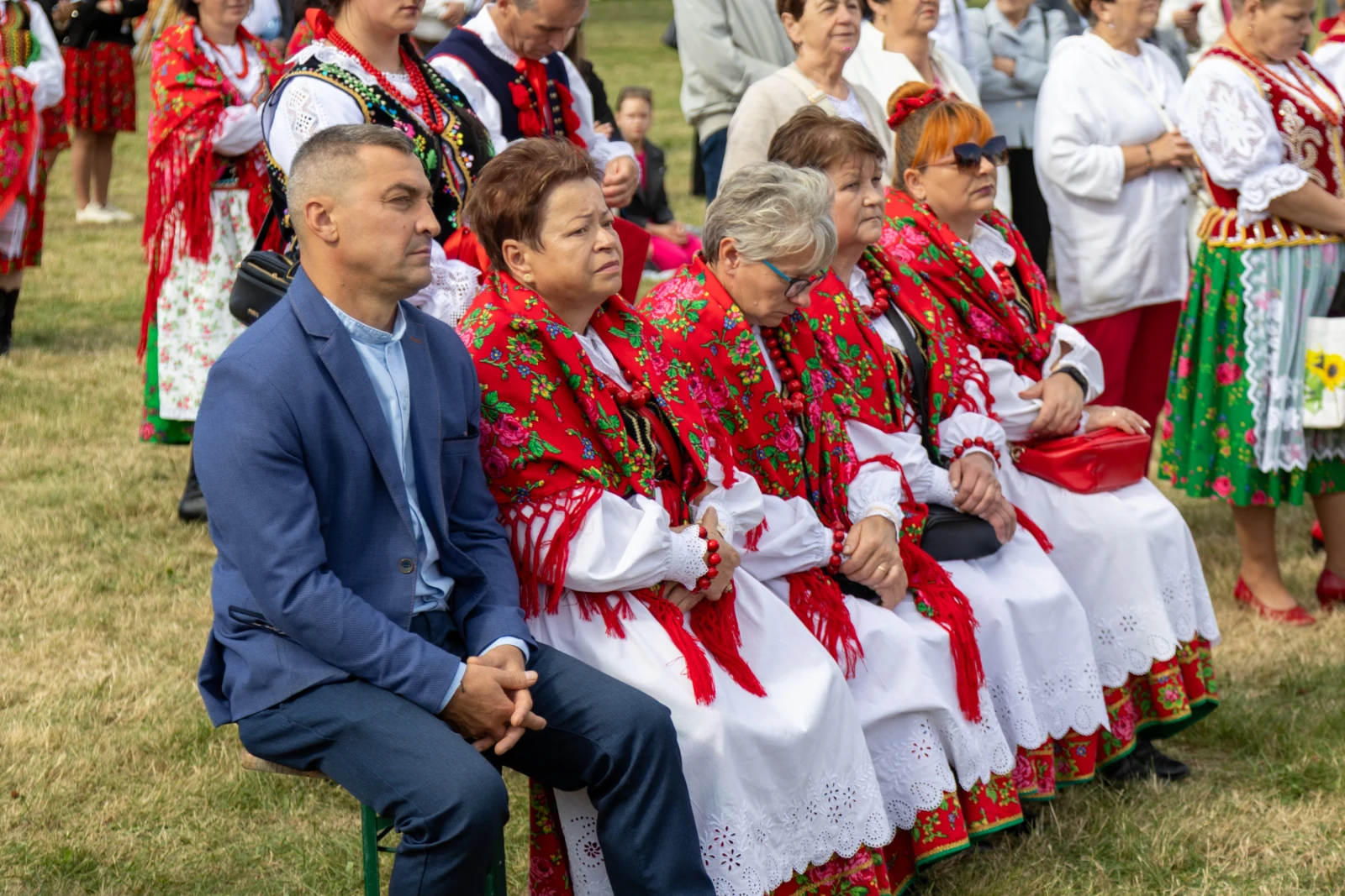 Grupa osób w tradycyjnych strojach ludowych siedzących na trawie podczas wydarzenia.  Autor: Bogusław Świerzowski