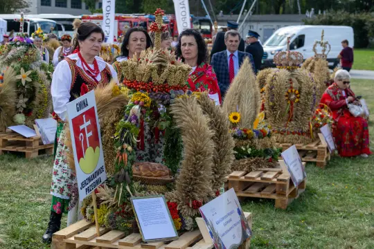Kobiety w tradycyjnych strojach ludowych przy dekoracjach zbożowych na festiwalu.