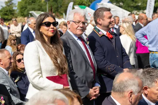 Grupa ludzi w eleganckich strojach, uczestniczących w wydarzeniu na świeżym powietrzu.