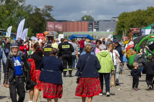 Tłum ludzi na festynie, w tle stoiska i pojazdy rolnicze.