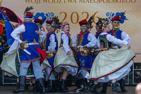 Grupa tancerzy w tradycyjnych strojach ludowych tańczy na scenie.