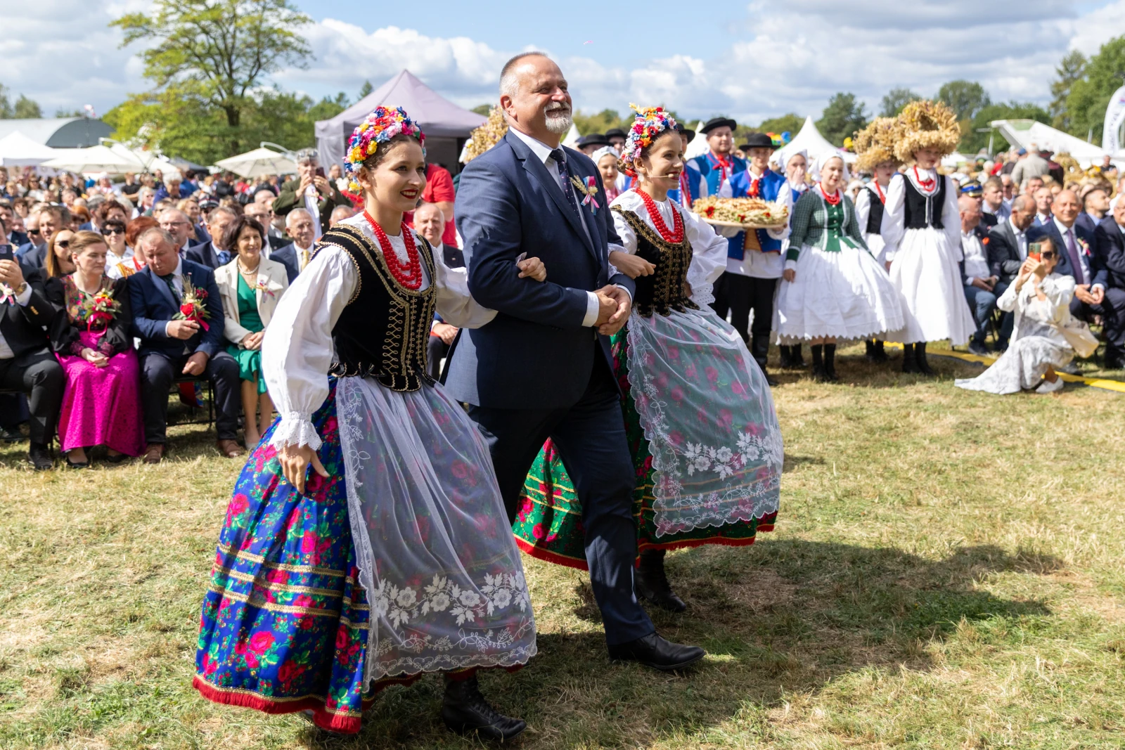 Mężczyzna w garniturze idzie w towarzystwie kobiet w tradycyjnych strojach ludowych.  Autor: Bogusław Świerzowski