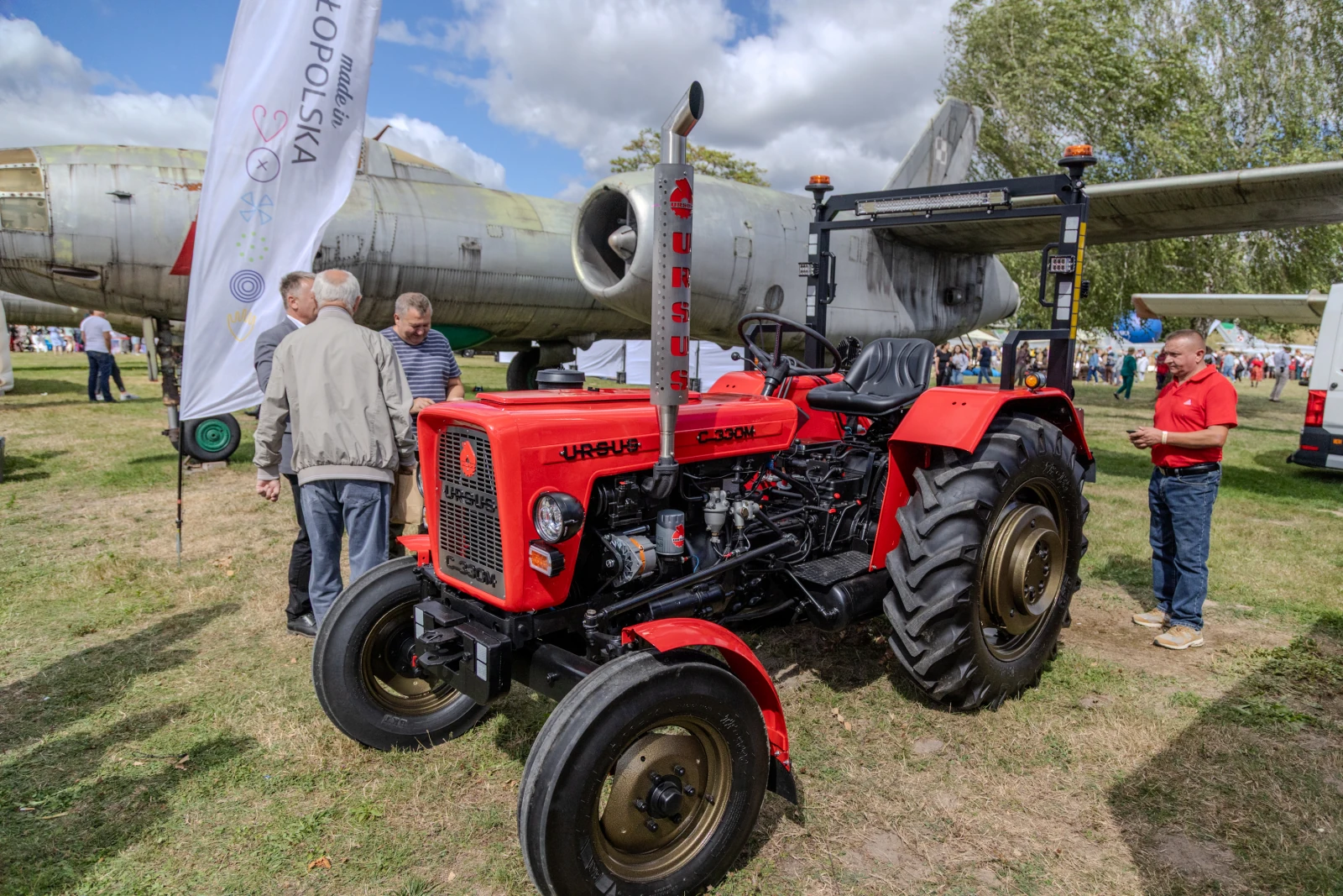 Czerwony traktor Ursus obok samolotu, ludzie w tle, wydarzenie plenerowe.  Autor: Bogusław Świerzowski