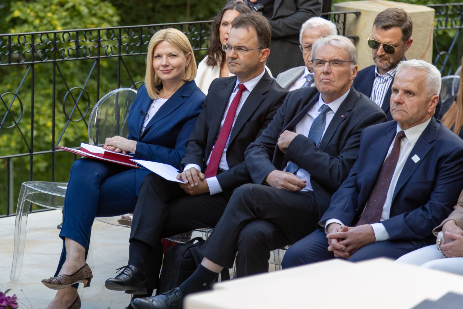 Grupa osób siedzących na wydarzeniu, w formalnych strojach, z poważnymi wyrazami twarzy.  Autor: Bogusław Świerzowski