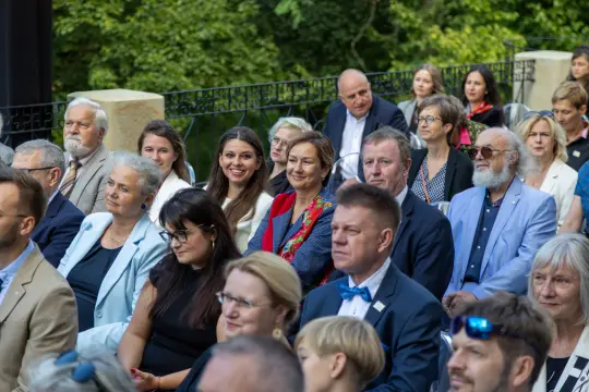 Grupa ludzi siedzących na wydarzeniu, wśród nich kobiety i mężczyźni w eleganckich strojach.