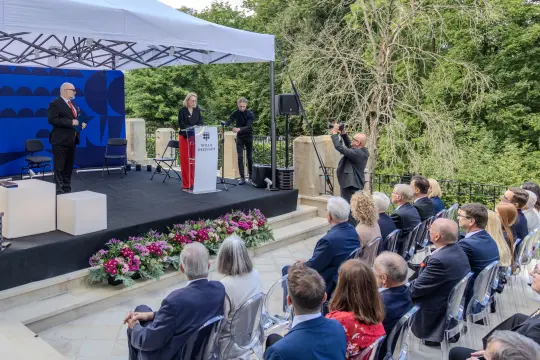 Konferencja na świeżym powietrzu z mówcami i publicznością, otoczenie zieleni.