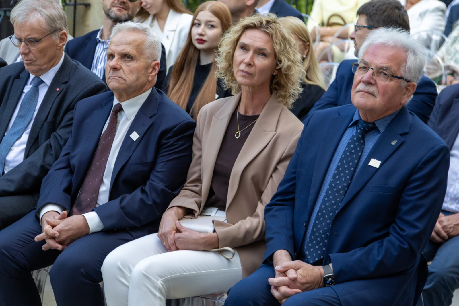 Grupa osób siedzących na wydarzeniu, wśród nich kobieta w jasnym garniturze i mężczyźni w eleganckich strojach.  Autor: Bogusław Świerzowski