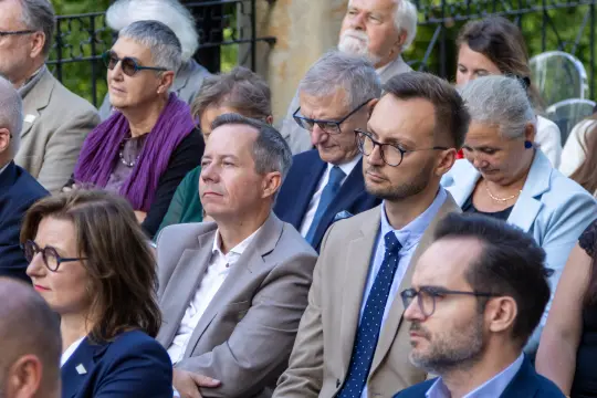 Grupa ludzi w eleganckich strojach, uczestniczących w wydarzeniu na świeżym powietrzu.