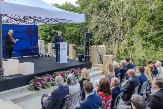 Uroczystość na świeżym powietrzu z mówcą przy podium i słuchaczami.