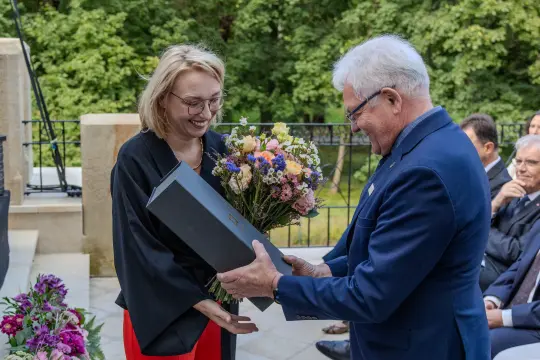 Kobieta w okularach przyjmuje bukiet kwiatów od mężczyzny w garniturze.