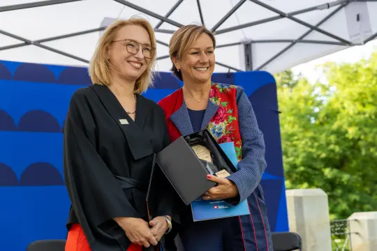 Dwie kobiety uśmiechają się, trzymając nagrodę w eleganckim otoczeniu.