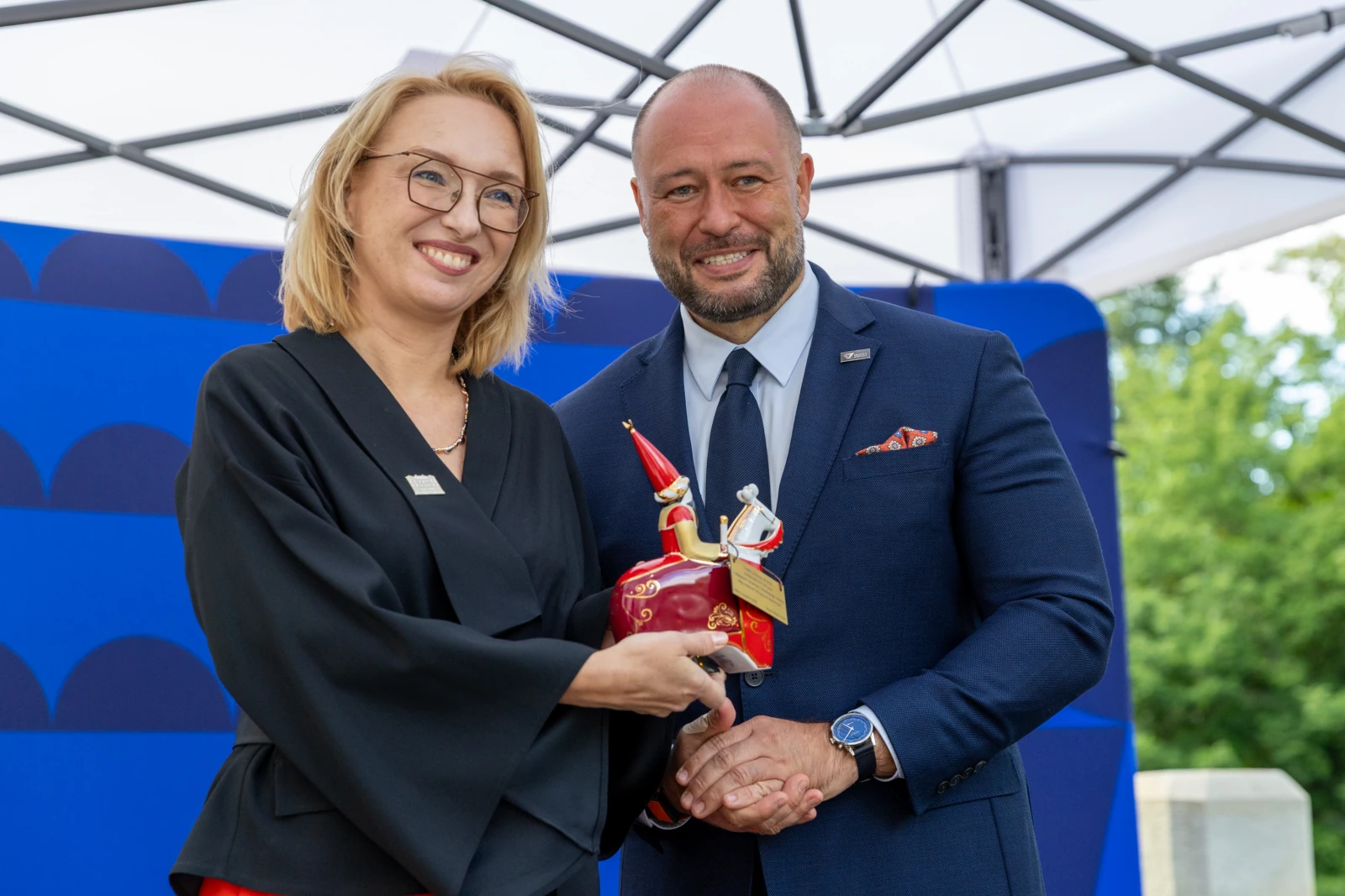Wręczenie nagrody przez uśmiechnięte osoby, trzymające trofeum w kształcie statuetki.  Autor: Bogusław Świerzowski