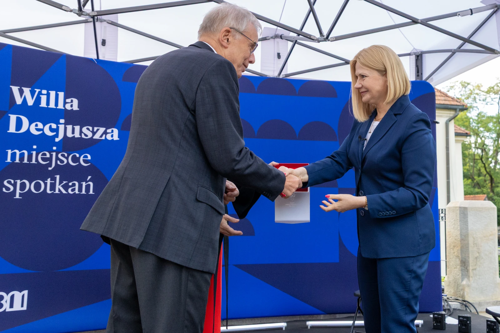 Uroczystość wręczenia dokumentu w Willi Decjusza. Mężczyzna i kobieta podają sobie ręce.  Autor: Bogusław Świerzowski