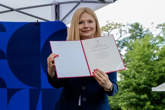 Kobieta trzyma dokument z pieczęcią, uśmiechając się do kamery.