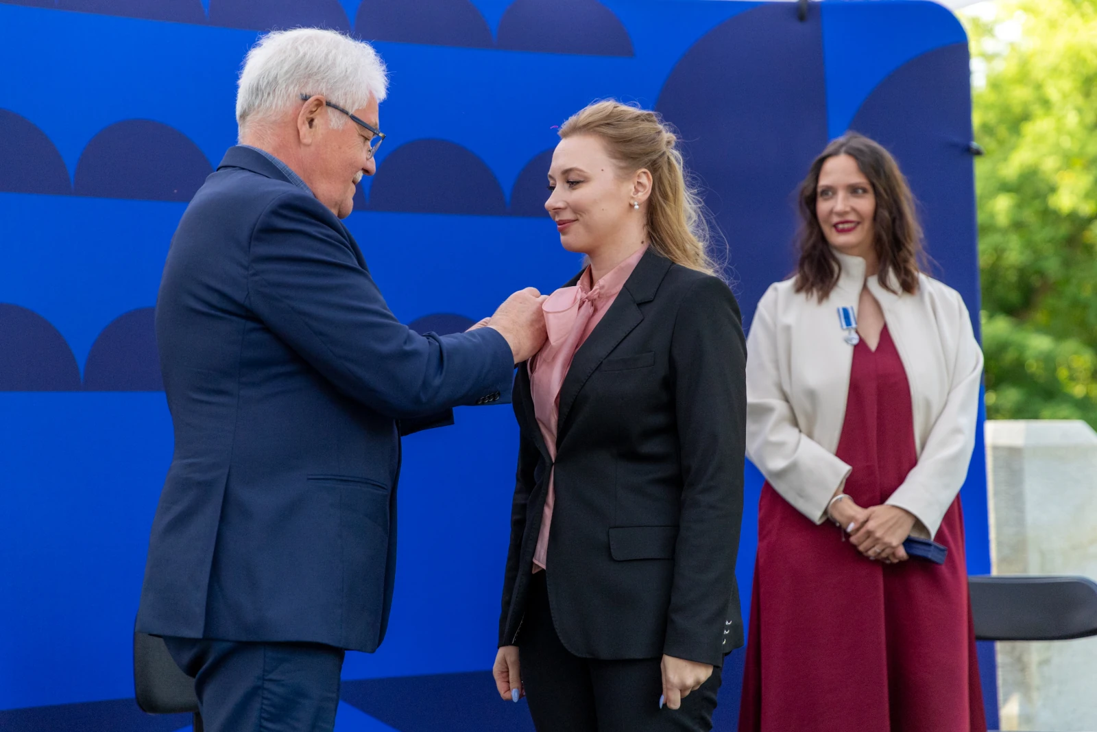 Wręczenie odznaczenia kobiecie przez mężczyznę, w tle inna kobieta.  Autor: Bogusław Świerzowski