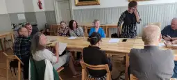 Grupa osób siedzących przy stole, prowadząca dyskusję lub spotkanie.
