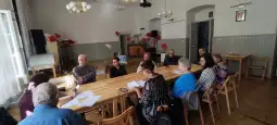 Grupa osób siedzących przy stole w sali z jasnym oświetleniem, prowadząca dyskusję.