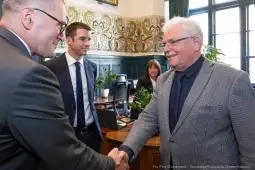 Spotkanie dwóch mężczyzn przy uścisku dłoni w biurze, w tle kobieta i rośliny.