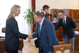 Spotkanie dwóch osób przy uścisku dłoni w biurze. W tle meble biurowe i rośliny.