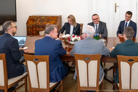 Spotkanie przy stole w sali konferencyjnej, uczestnicy rozmawiają i omawiają sprawy.