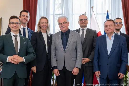 Grupa osób w formalnych strojach, pozująca do zdjęcia w biurze.