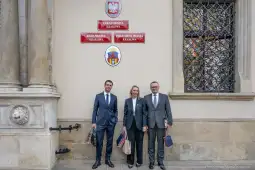 Trzy osoby w eleganckich strojach stoją przed budynkiem Urzędu Miasta Krakowa.
