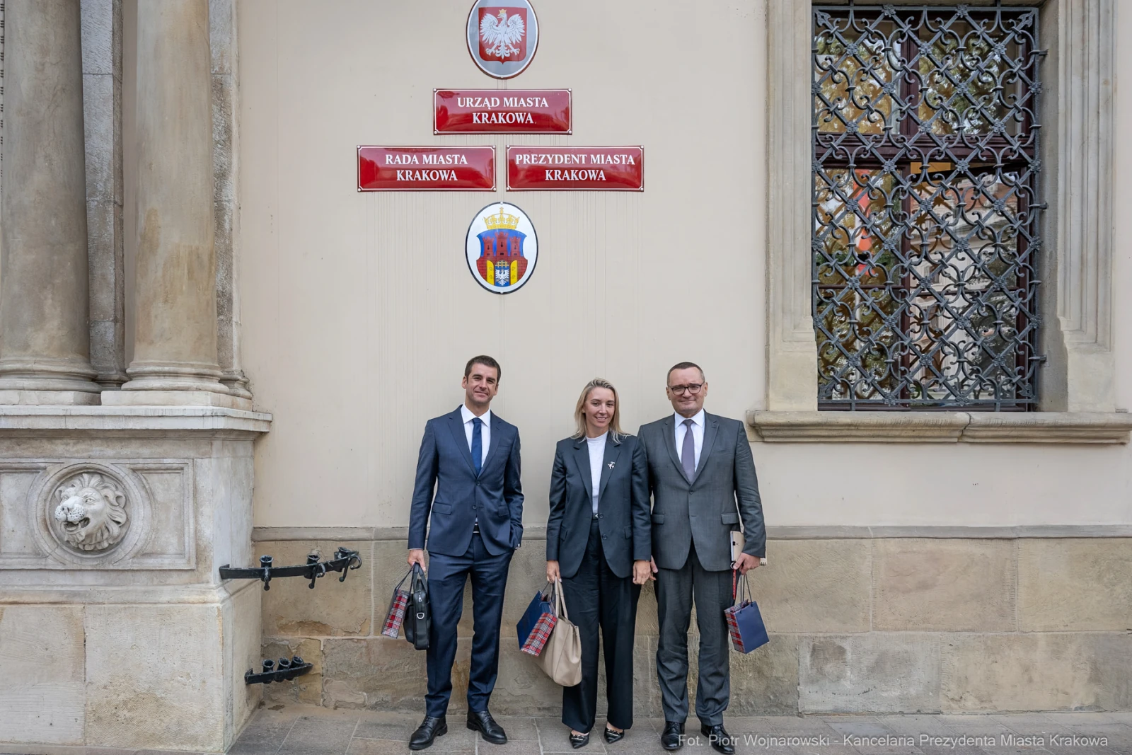 Trzy osoby w eleganckich strojach stoją przed budynkiem Urzędu Miasta Krakowa.  Autor: Piotr Wojnarowski