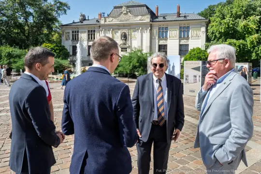 Czterech mężczyzn rozmawia na tle historycznego budynku.