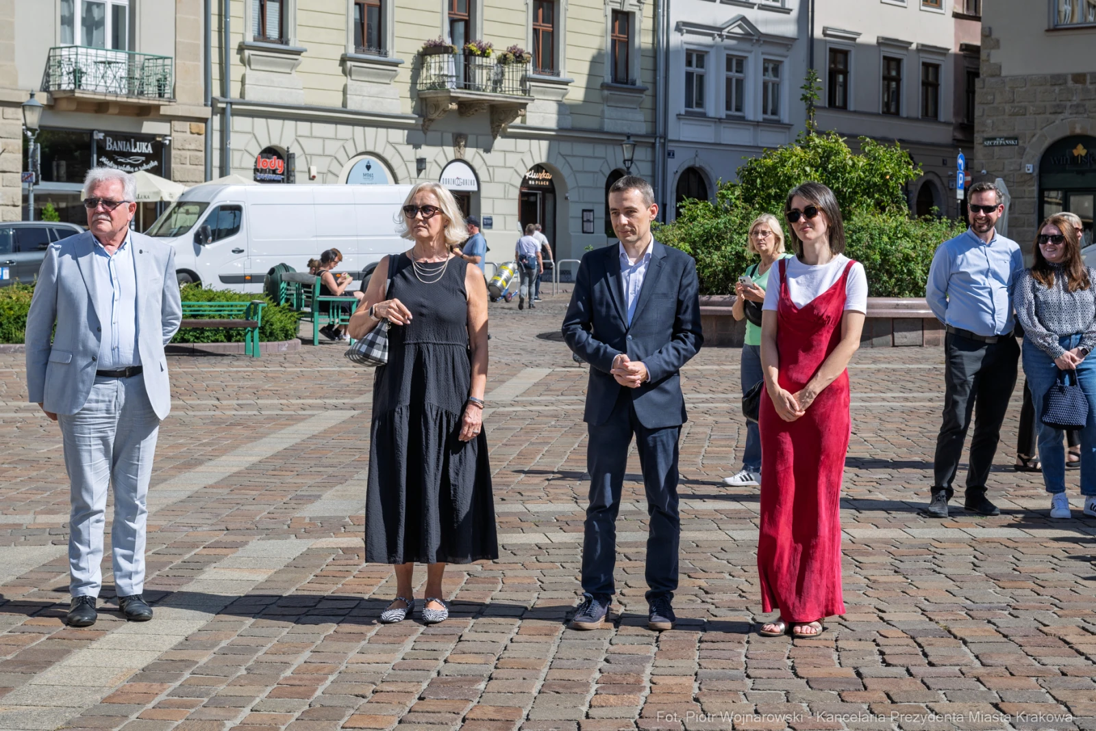 Cztery osoby stojące na placu, w tle budynki i zieleń.  Autor: Piotr Wojnarowski