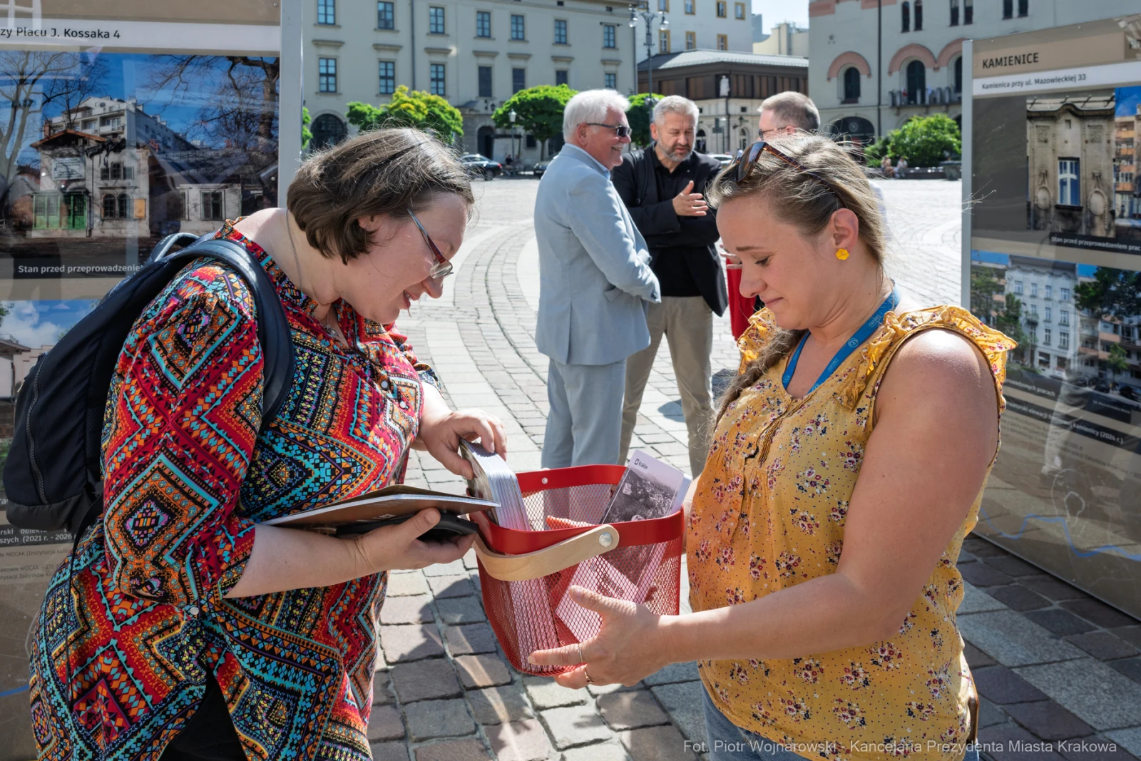 Dwie kobiety rozmawiają i przeglądają materiały w przestrzeni publicznej. W tle inni ludzie.  Autor: Piotr Wojnarowski