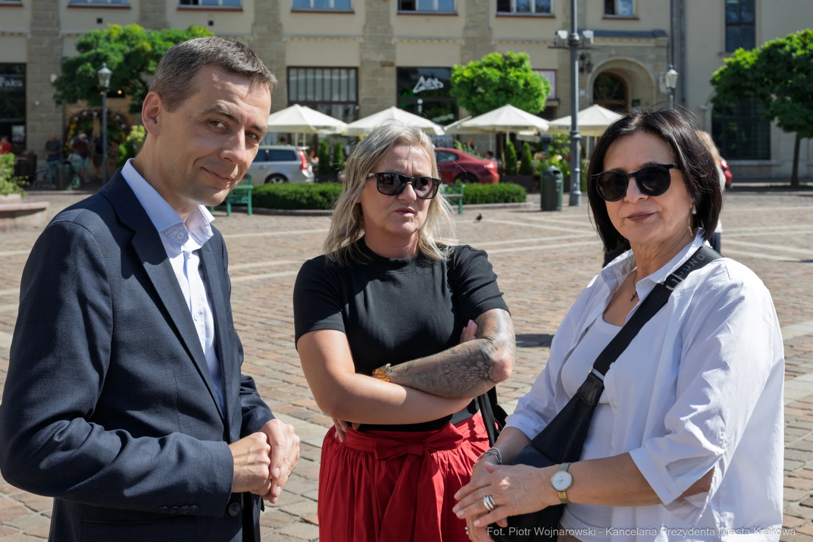 Trzy osoby na placu, dwie kobiety i mężczyzna, rozmawiają w słoneczny dzień.  Autor: Piotr Wojnarowski