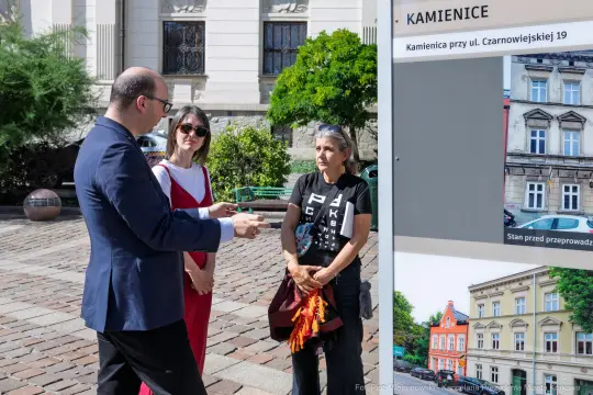 Grupa ludzi rozmawia obok tablicy informacyjnej o kamienicach przy ul. Czarnowiejskiej 19.