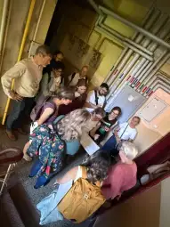 Grupa ludzi zbiera się wokół stołu, przeglądając dokumenty w korytarzu.