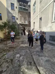 Grupa ludzi w podwórku, rozmawiających i stojących obok budynków.