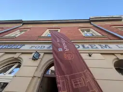Budynek z historycznym napisem i flagą reklamową.