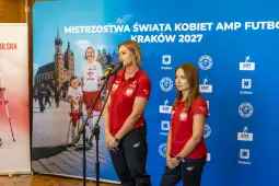 Dwie kobiety w czerwonych koszulkach reprezentacyjnych podczas konferencji prasowej.