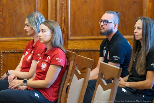 Cztery osoby w strojach sportowych siedzą w sali, skupione na wydarzeniu.